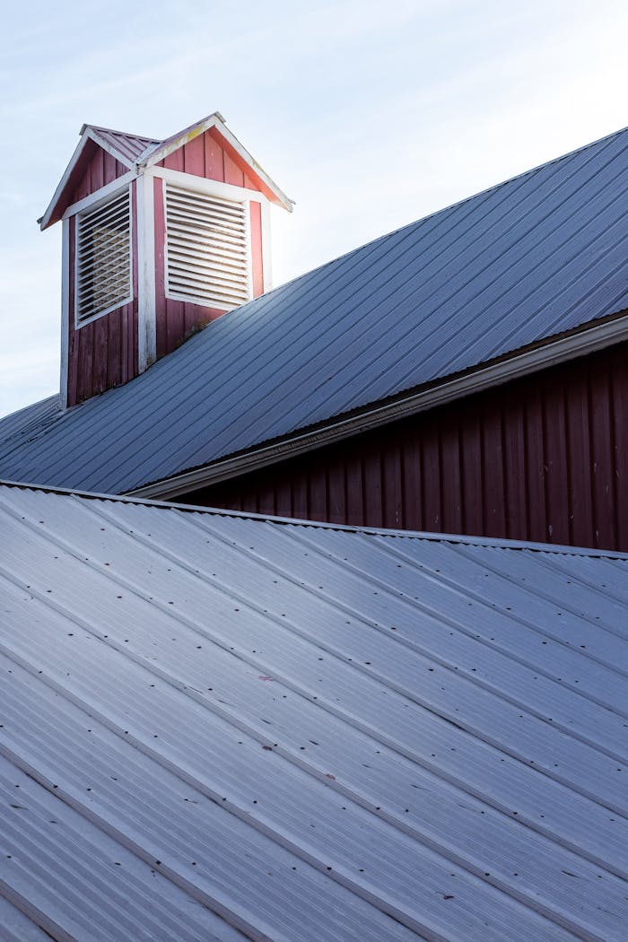 Close-up of a textured metal rooftop featuring a red vent structure, captured at sunset enhancing shadows.